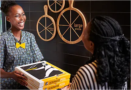 Debonairs Pizza employee handing pizza takeaway boxes to a customer